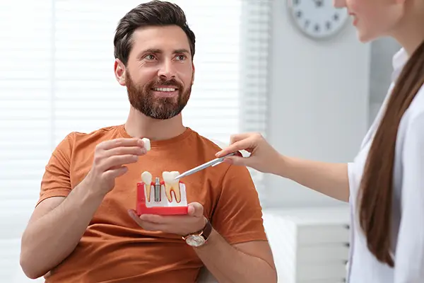 A patient holds a model of teeth with a single dental implant, while discussing implant benefits with his dentist.